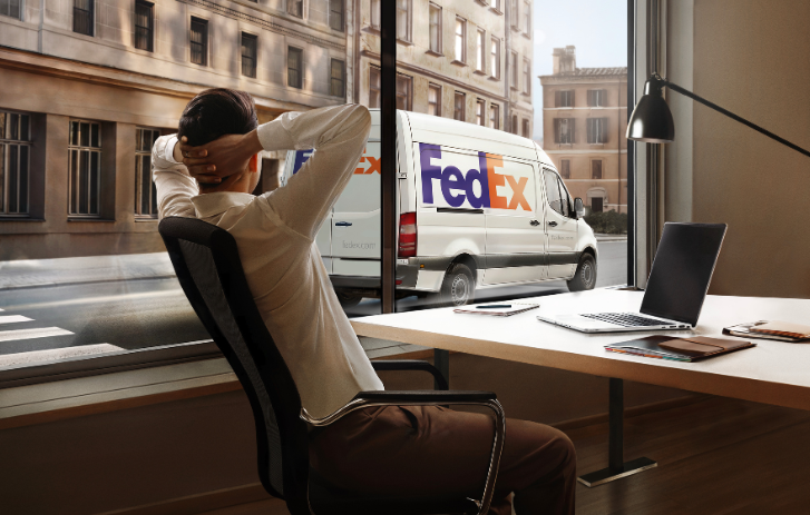Man leaning back in chair with FedEx van in background on the street