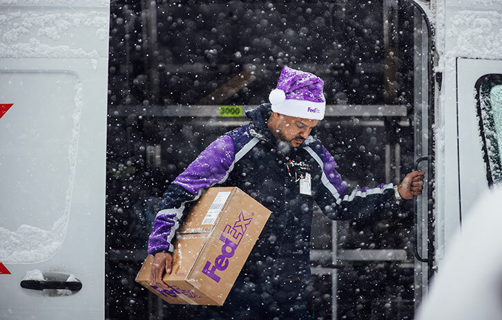 FedEx darbinieks izkāpj no furgona, nesot paku sniegā