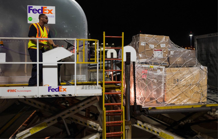 FedEx employee loading cargo onto a FedEx plane